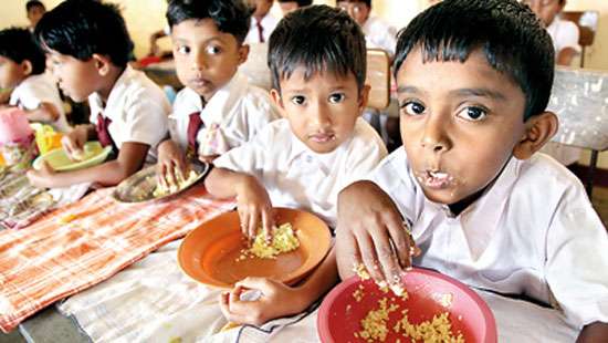 Schoolchildren in white uniforms eating a rice meal from bowls at their classroom desks