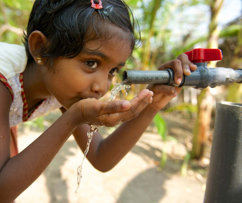 A young girl drinking from an outdoor tap, cupping the running water in her hand